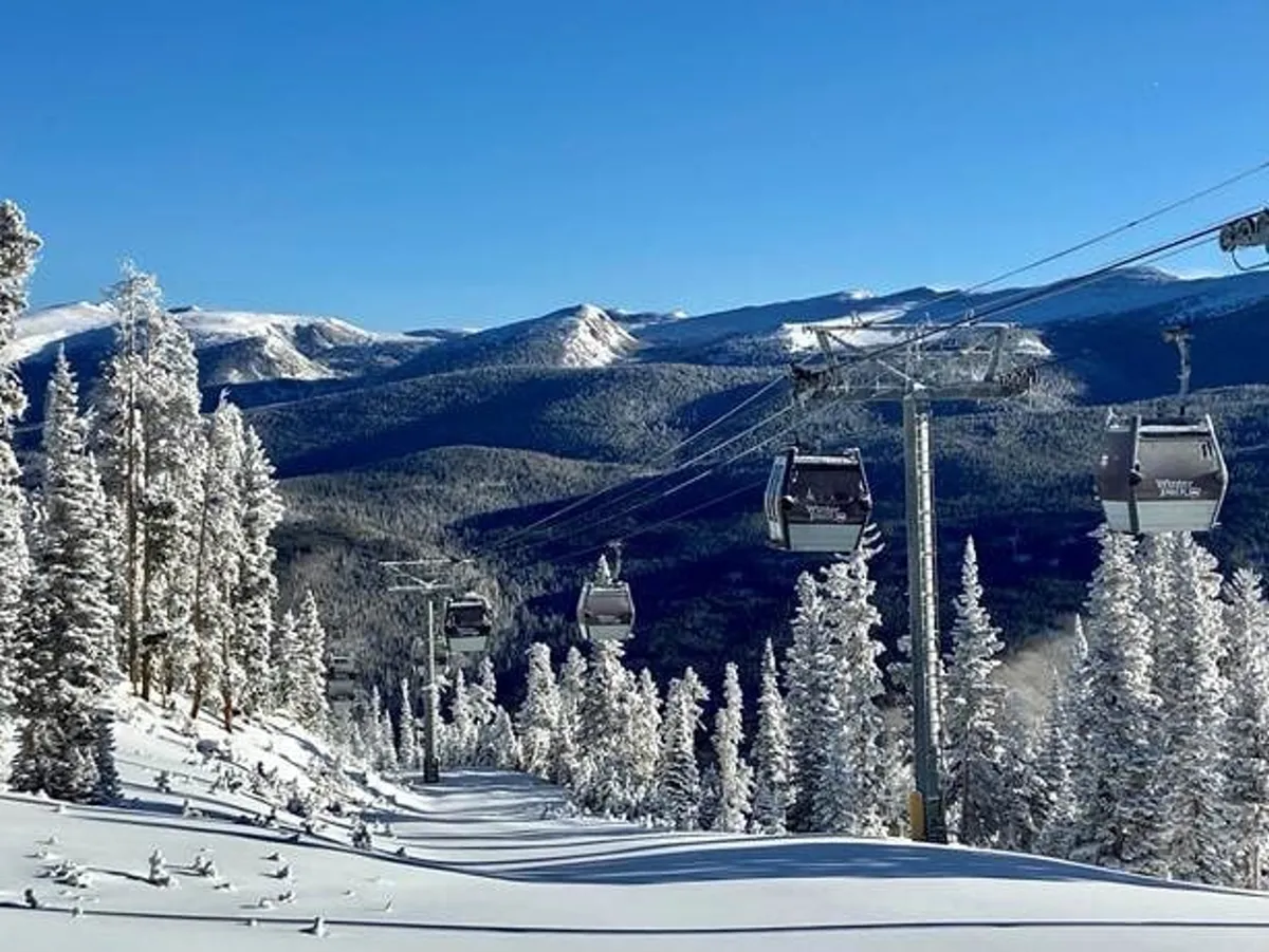 A wintery landscape with gondola lifts gliding above snow-covered hills, surrounded by pine trees and framed by distant mountain peaks. The scene suggests easy access to snow sports and adventure, typical of a luxury mountain destination.