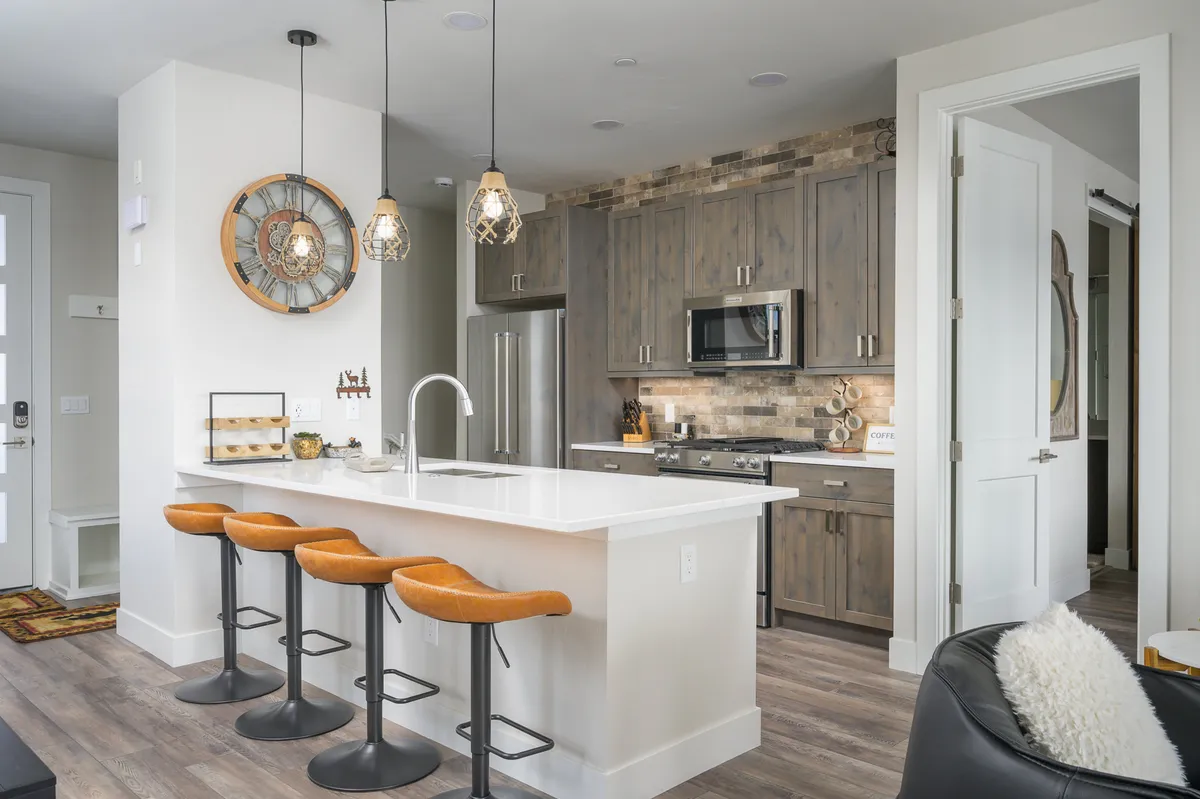 A sleek chef’s kitchen anchors the space, featuring a large island with bar stools, modern appliances, and stylish accents like a decorative wall clock. The kitchen is designed for both functionality and social interaction, inviting guests to gather while meals are prepared.