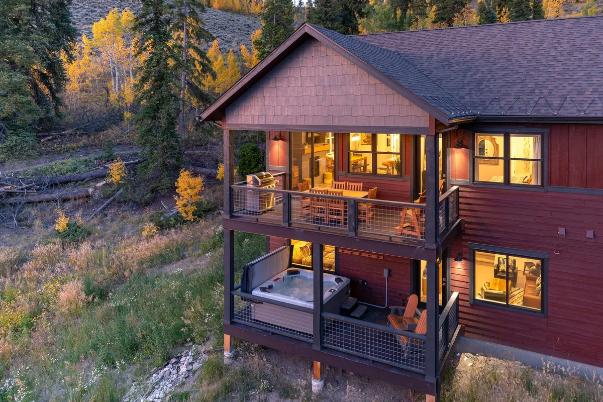A cozy outdoor hot tub nestled on a spacious deck with sweeping river and mountain views visible through large windows. The hot tub is surrounded by comfortable seating, perfect for stargazing or unwinding after a day of adventure.