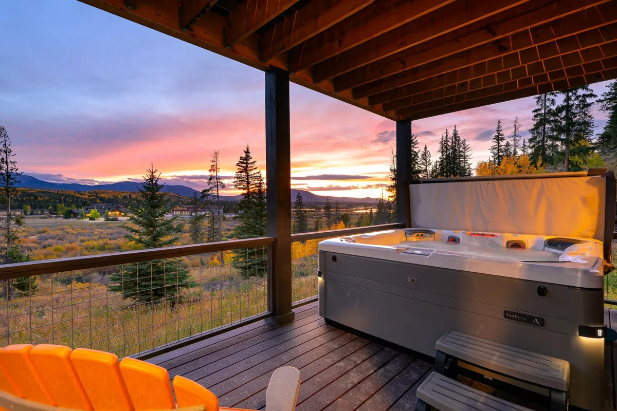 An inviting outdoor hot tub set against a sunset sky, with panoramic mountain views in the background. The scene captures the experience of soaking under the stars after an active day, connecting interior fun with outdoor relaxation.