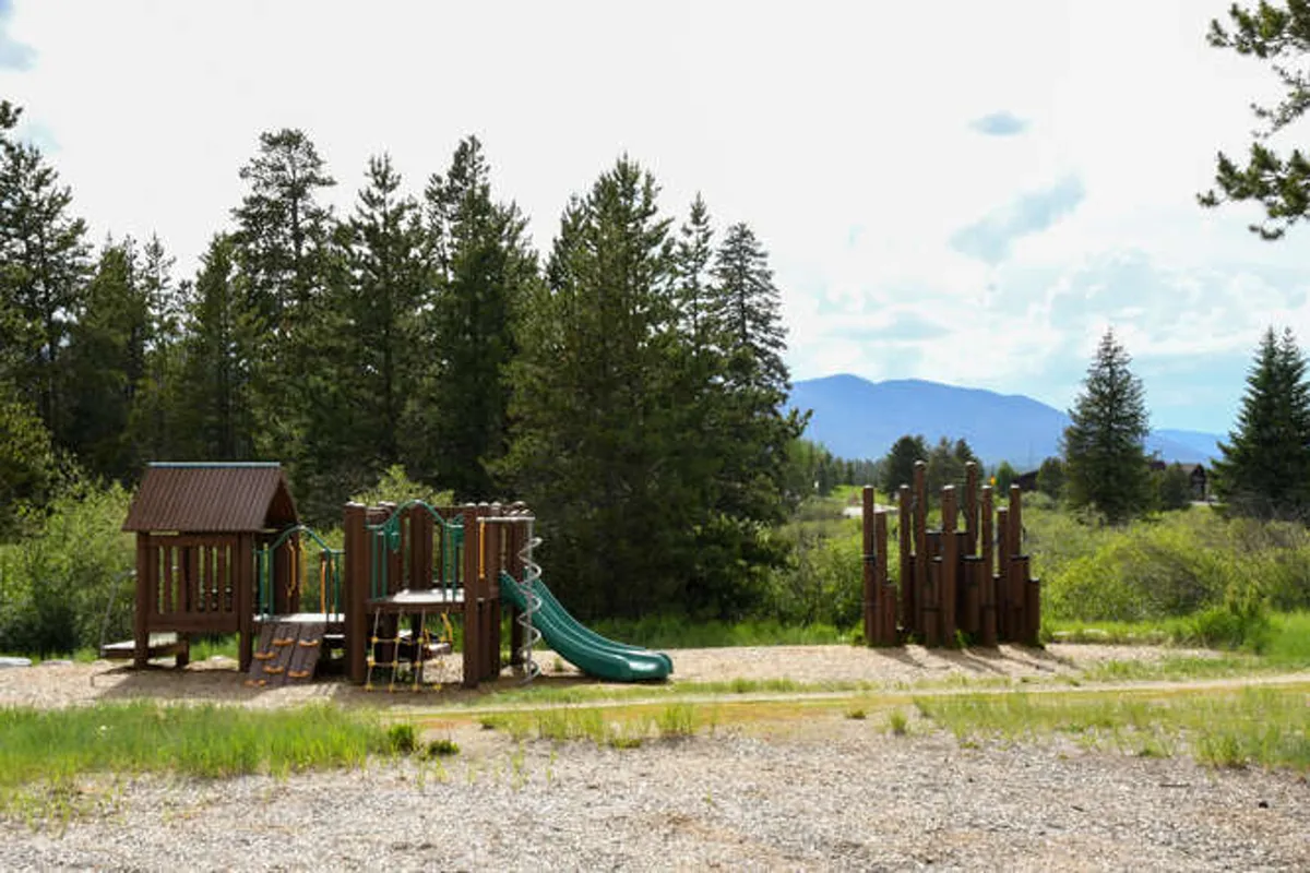 A cheerful exterior image focused on a playground nestled among trees, with children playing on slides and swings. The surrounding greenery and open space create a welcoming and safe environment for families.