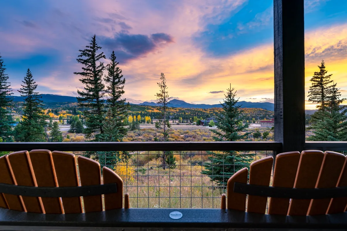 Balcony chairs arranged to face a dramatic sunset sky and panoramic mountain vistas, framed by pine trees. The tranquil setting invites relaxation, stargazing, or enjoying a glass of wine after a day outdoors.