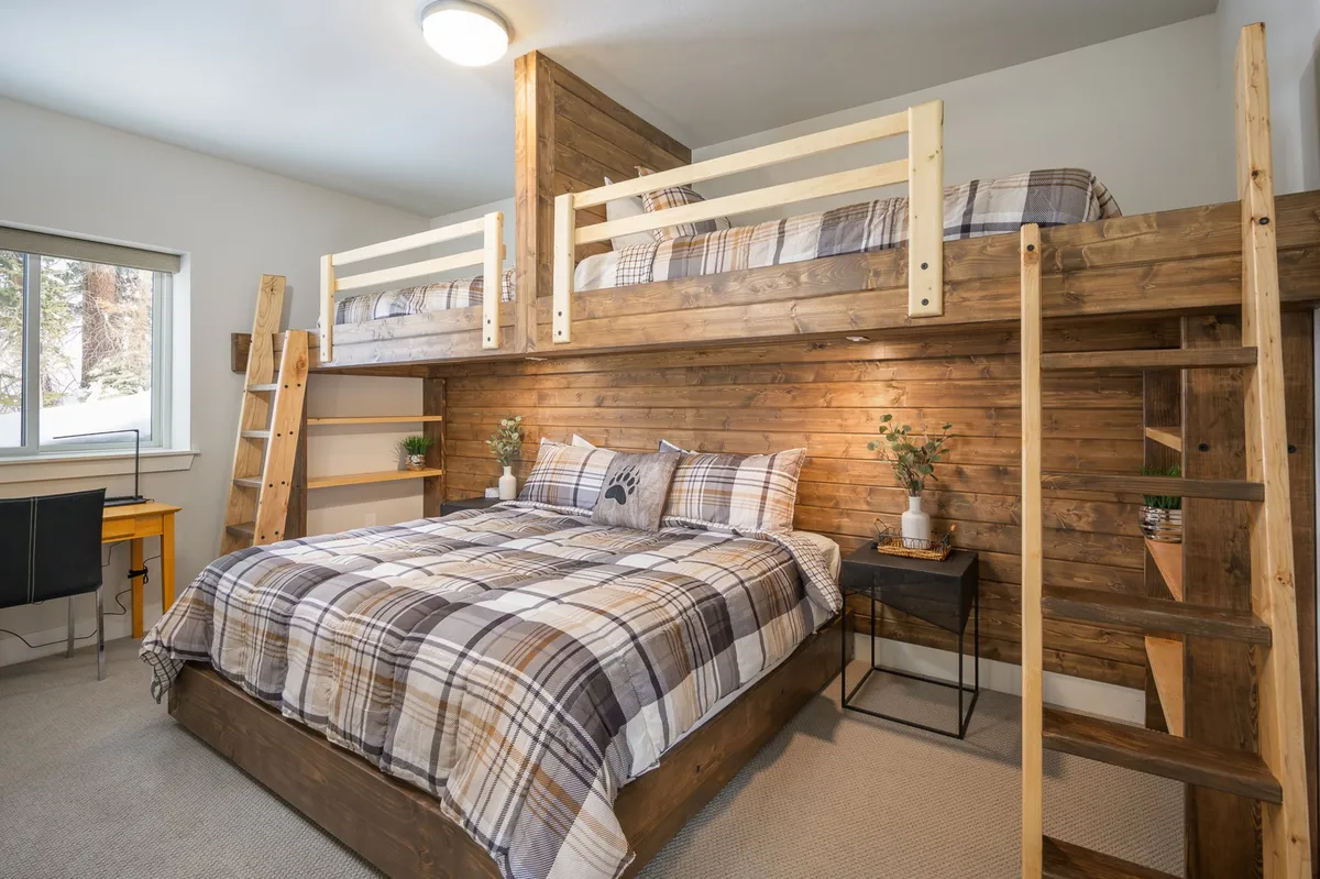 A cheerful interior featuring bunk beds with plaid bedding, wooden walls, and a desk area. The room’s ambiance is warm and inviting, providing the perfect backdrop for children’s laughter and playful sleepovers, as well as family bonding over games or shared stories.