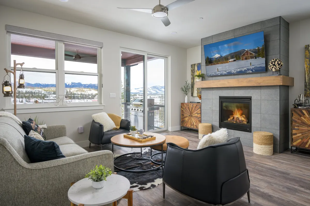 The great room features plush seating arranged around a striking stone fireplace, with expansive windows framing breathtaking views of the mountains. The space feels both spacious and intimate, ideal for relaxing or entertaining. A television and tasteful décor complete the inviting, mountain-chic ambiance.