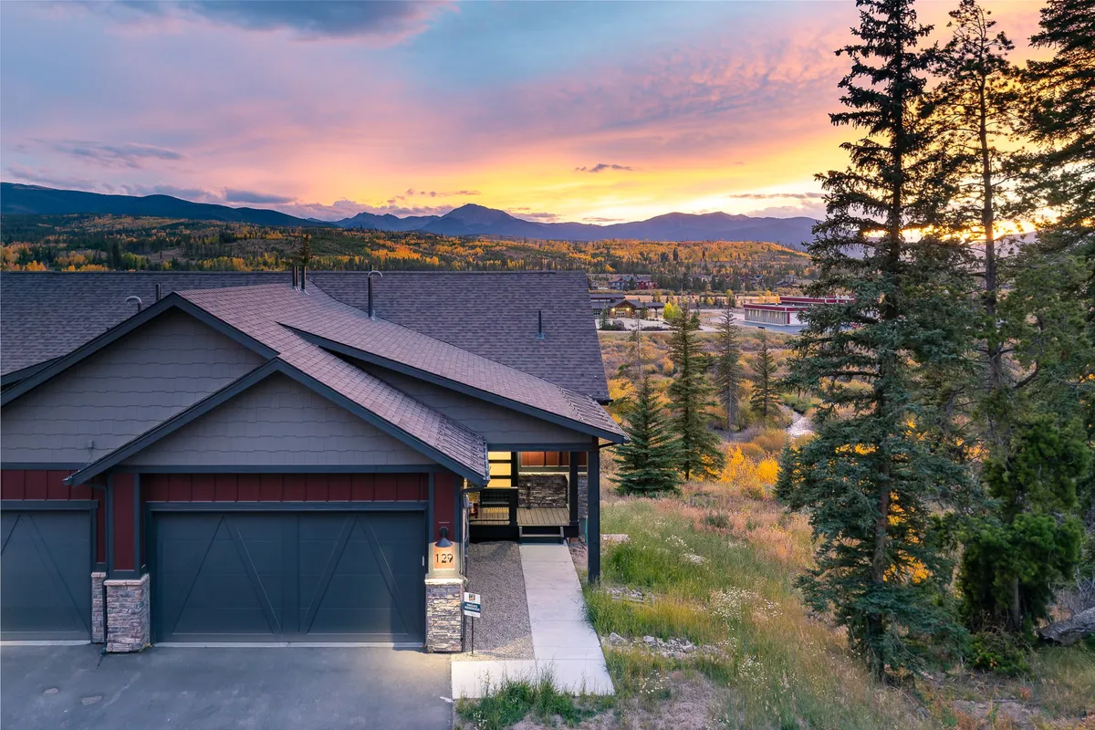 An inviting exterior shot at sunset, with mountains forming a dramatic backdrop behind a well-maintained property surrounded by lush greenery. The scene suggests immediate access to hiking and biking trails and is perfect for outdoor gatherings or evening relaxation after a day of adventure.
