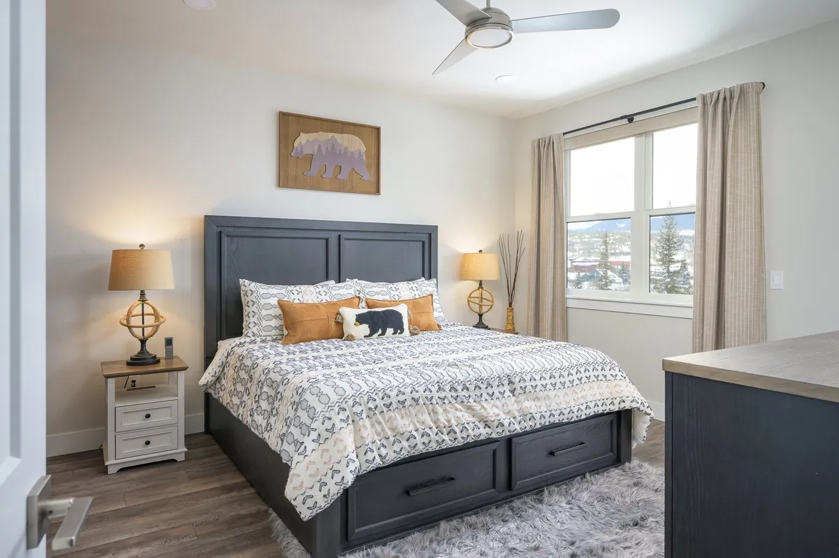 This image captures a tranquil bedroom featuring a comfortable bed adorned with decorative bear artwork above the headboard, flanked by stylish nightstands and a window that offers a scenic mountain view. The overall mood is serene, highlighting the restful ambiance and premium bedding.